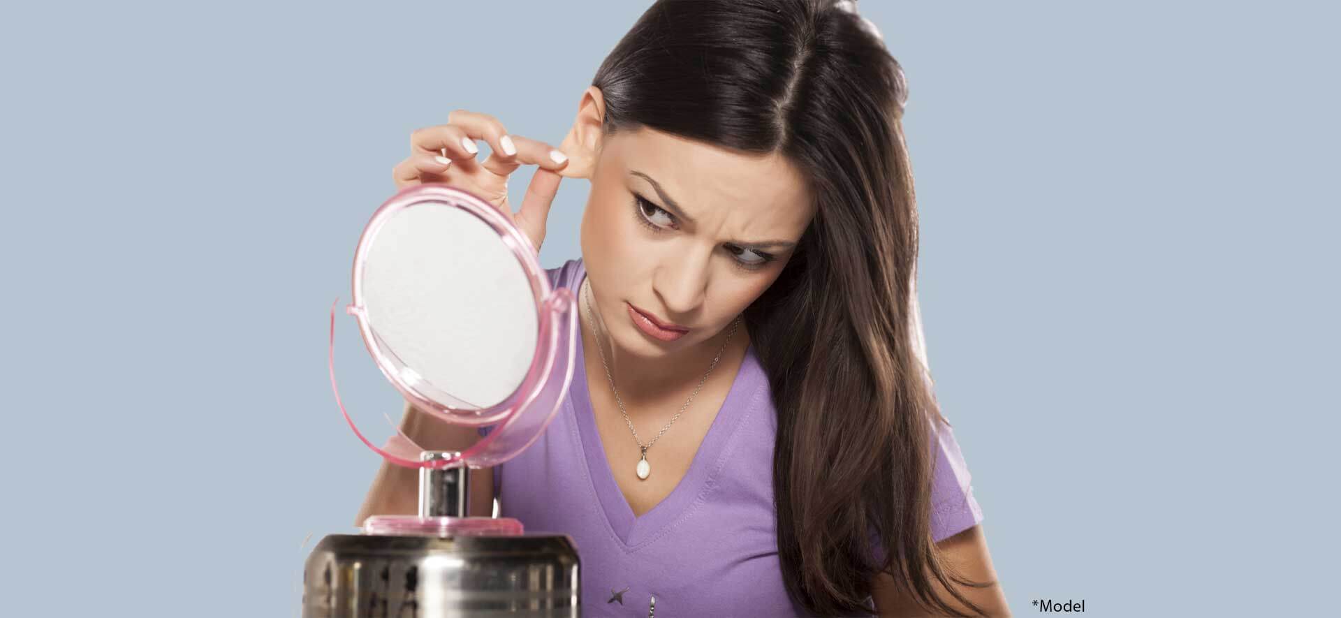 Girl pulling her ear with the fingers in front of a mirror