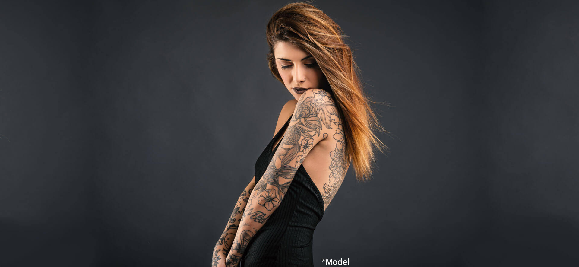 Intimate woman studio portrait with long black dress and tattoos against dark background
